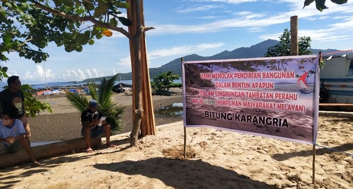 Baliho yang dipasang nelayan Karangria di lokasi proyek, berada di area tambatan perahu. (foto: ady/barta1)