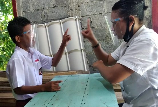 Ocen Hilda Lun mengajarkan bahasa isyarat saat belajar luring pada siswa tunarungu Meldo Malintoy di rumahnya